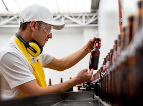 Worker inspecting bottles on a beverage production line.